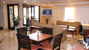 Habitación de hotel con zona de comedor, sofá, televisor montado en la pared y un amplio ventanal.
