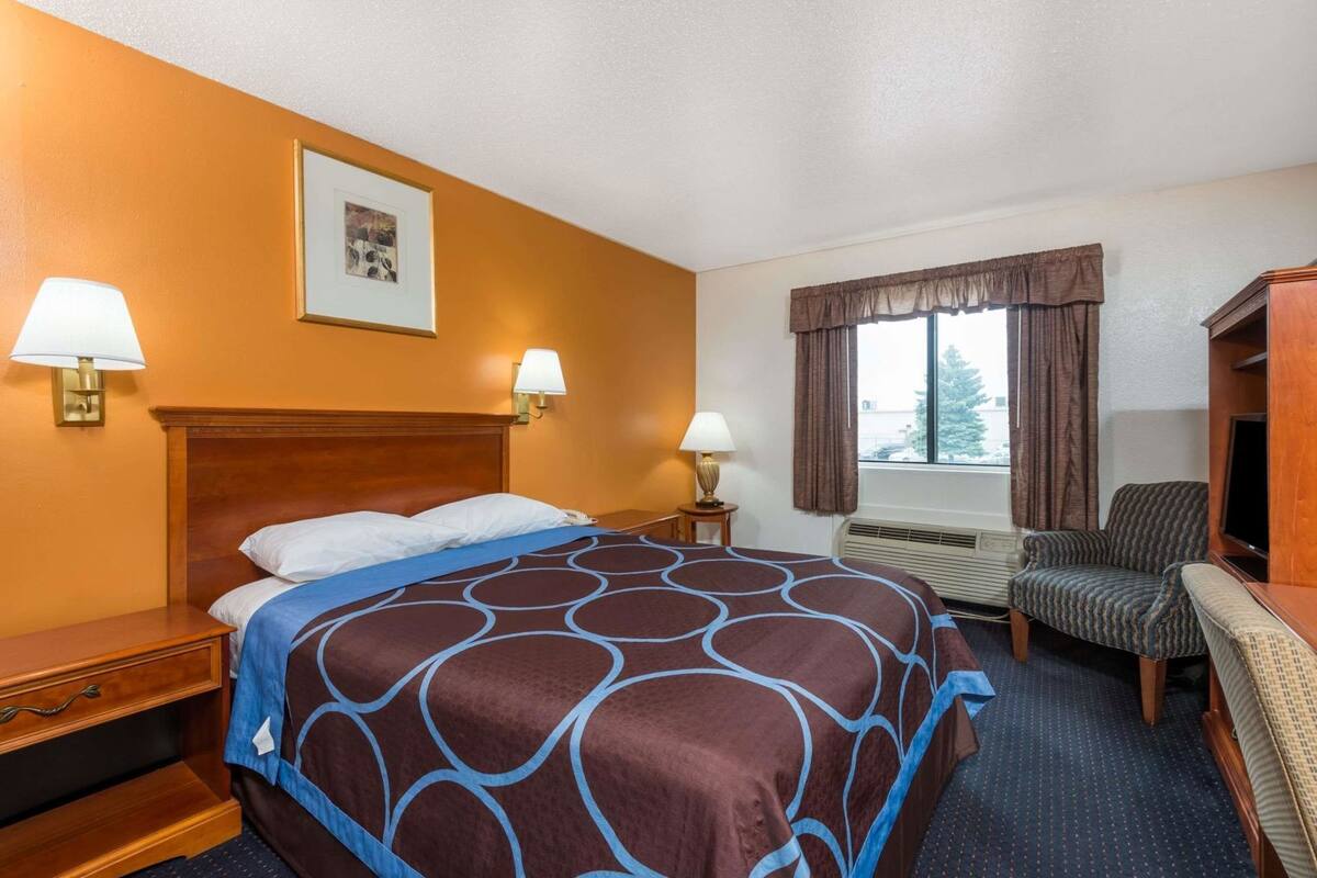 A hotel room with a large bed, two bedside lamps, a chair, a desk, and a window with curtains.