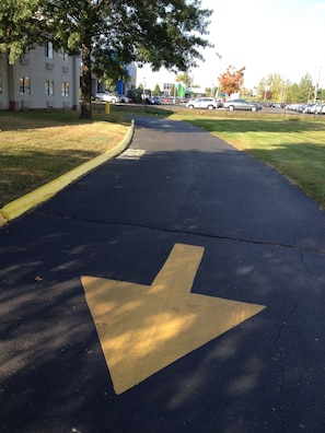 A parking lot with a directional arrow on the pavement, surrounded by grass and trees.