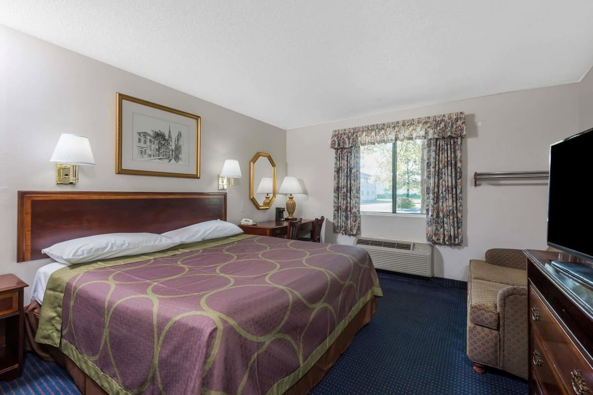 A hotel room with a large bed, a desk, a chair, a television, and a window with curtains.