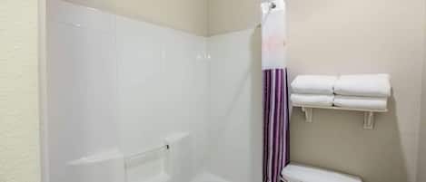 Et badeværelse med bruser, toilet og et håndklædestativ med foldede håndklæder.