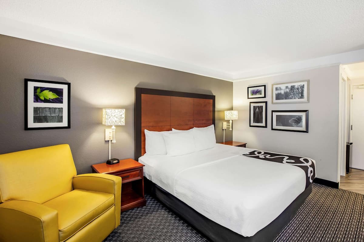 Een hotelkamer met een groot bed, een gele fauteuil, een houten nachtkastje en een muur met ingelijste foto's.