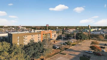 A hotel with a parking lot, surrounded by trees and a clear sky.
