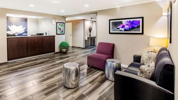 Un área de recepción con piso de madera, una mesa de recepción, un sillón rojo, un sofá y dos mesitas redondas.