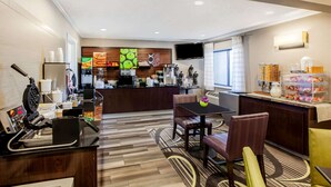 Un hall de hotel con barra de desayuno autoservicio, zona de estar y un televisor de pantalla plana montado en la pared.
