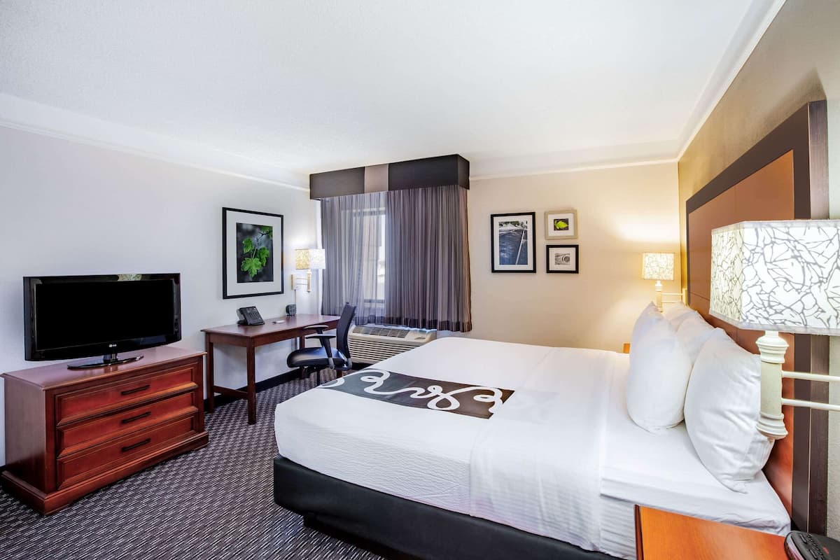 Een hotelkamer met een groot bed, een bureau met stoel, een televisie en een lamp.
