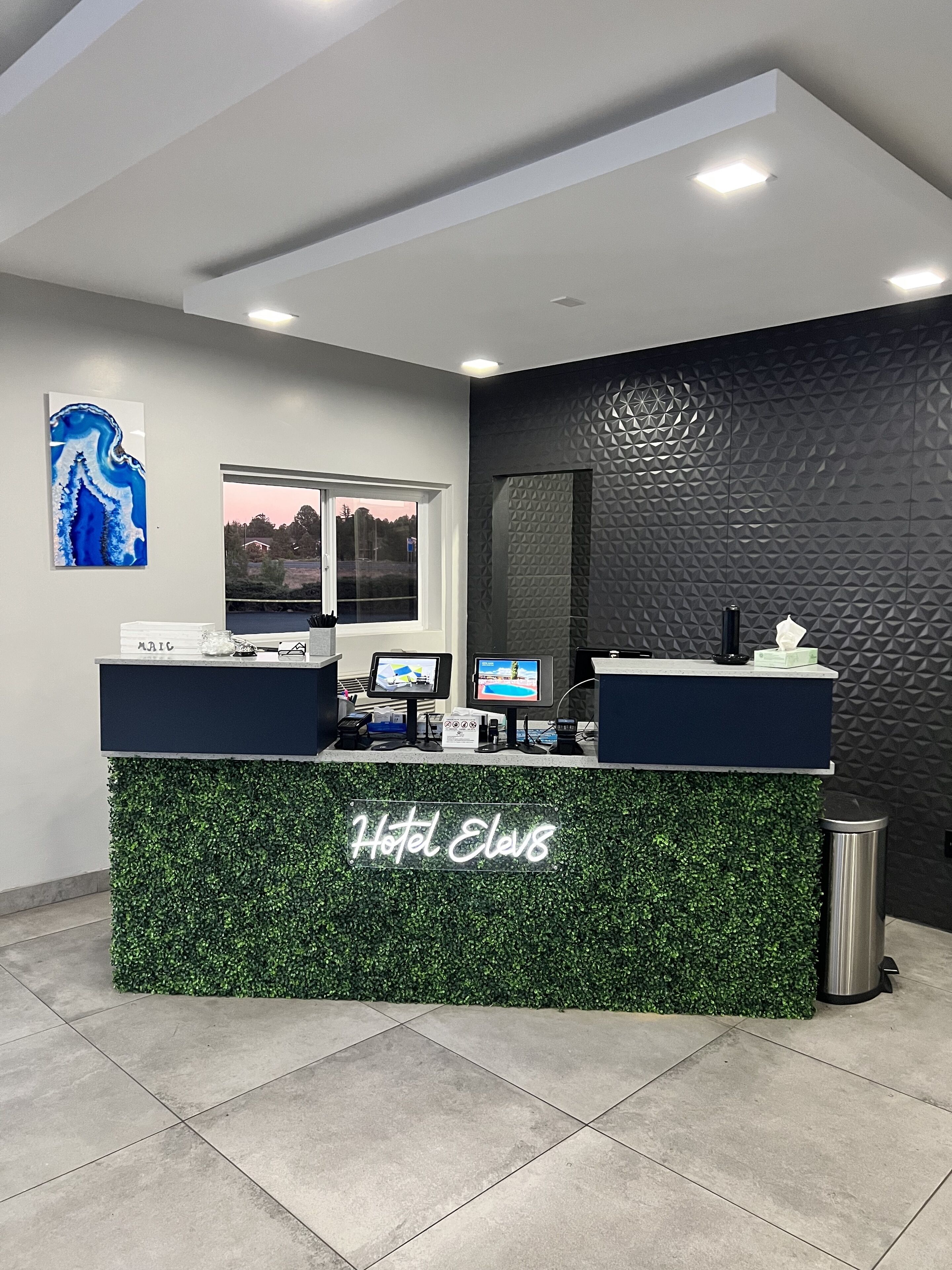Un comptoir d’accueil d’hôtel agrémenté d’un motif de feuillage vert, doté d’une grande fenêtre et présentant un intérieur moderne.