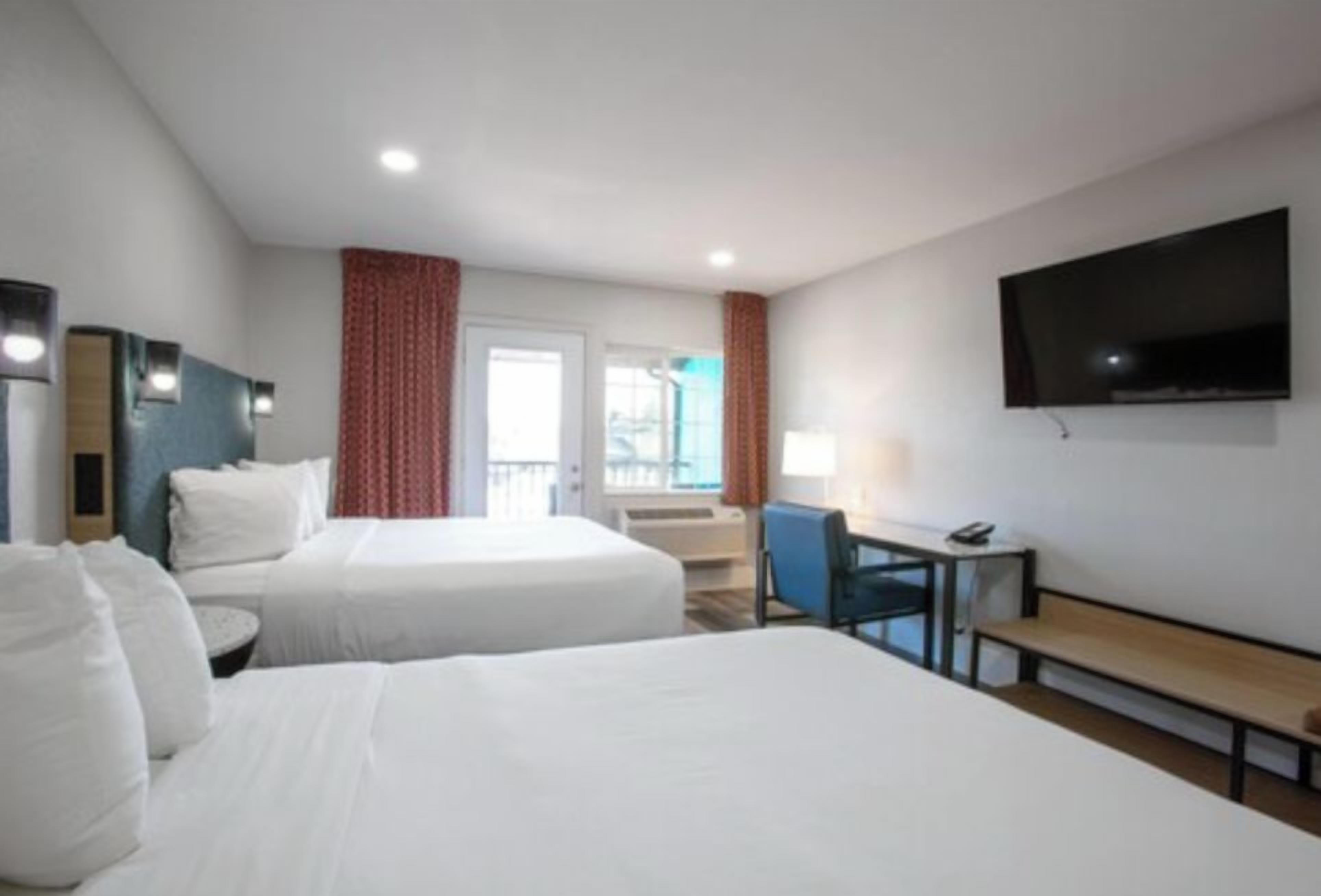 A hotel room with two beds, a desk, a chair, a TV, and a window with curtains.