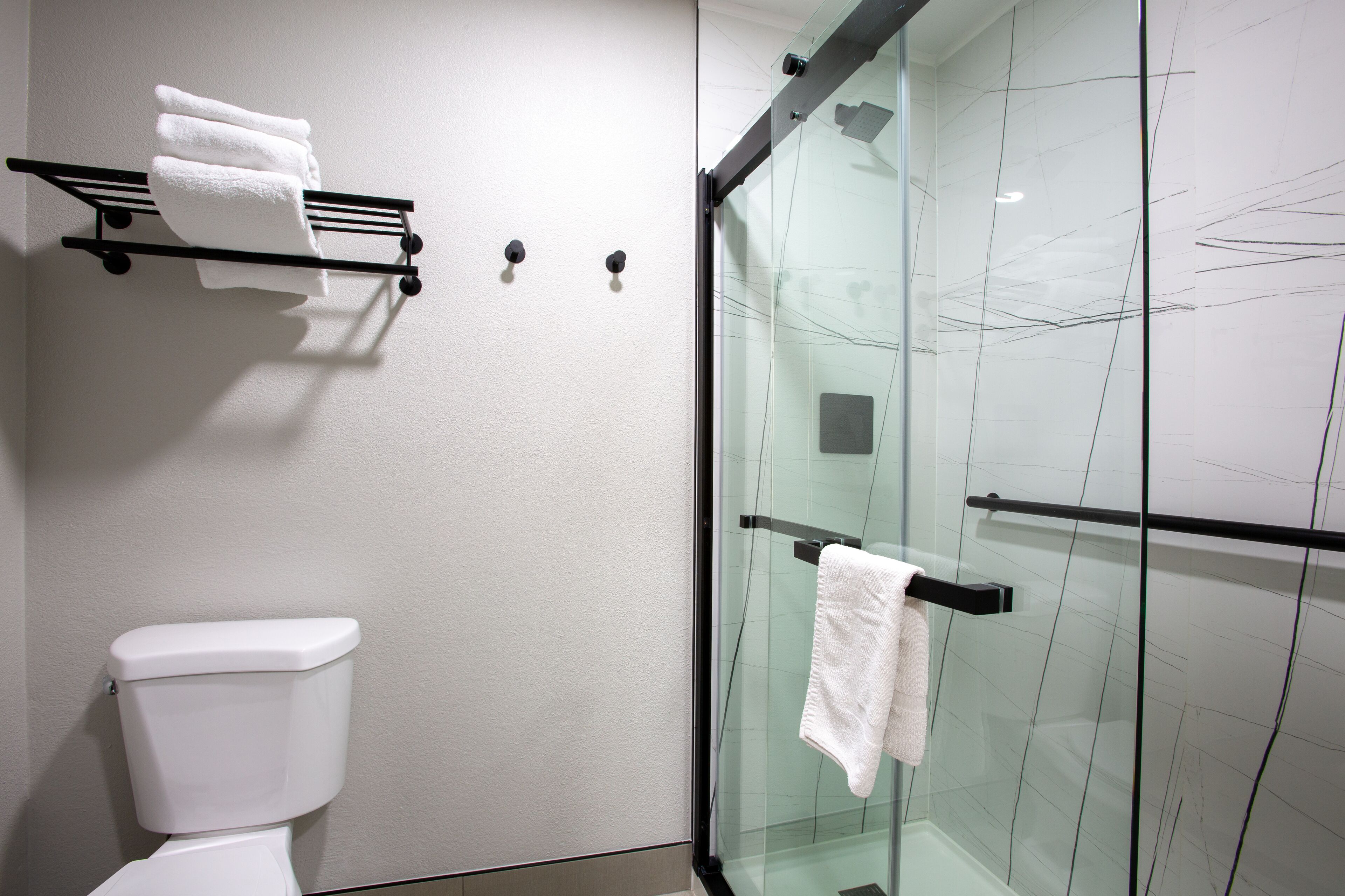 A modern bathroom with a glass shower enclosure, a white toilet, and a towel rack with multiple towels.