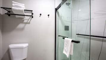 A modern bathroom with a glass shower enclosure, a white toilet, and a towel rack with multiple towels.