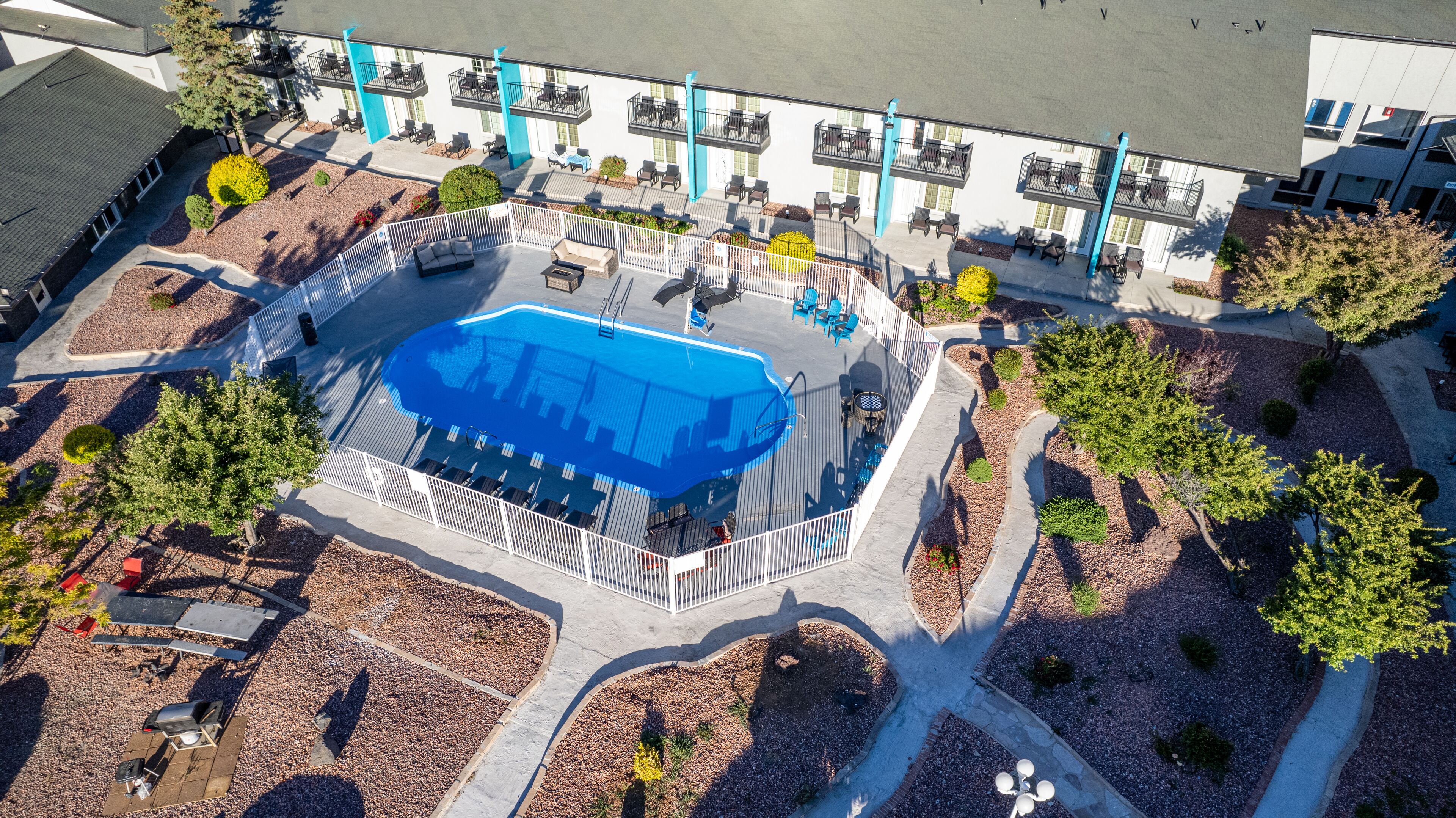 An aerial view of a hotel with a swimming pool, outdoor seating, and a landscaped garden.