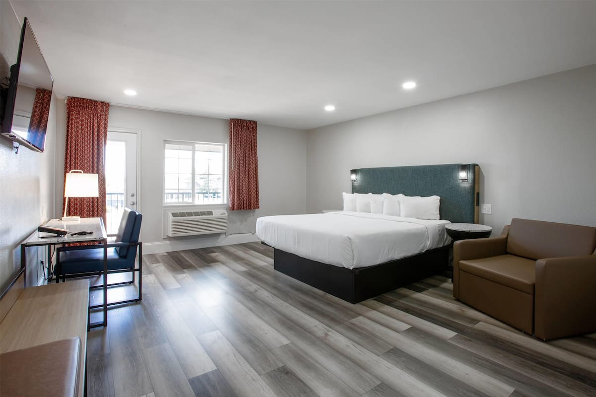 Ein Hotelzimmer mit einem Bett, einem Schreibtisch mit Stuhl, einer Couch und einem an der Wand befestigten Fernseher.