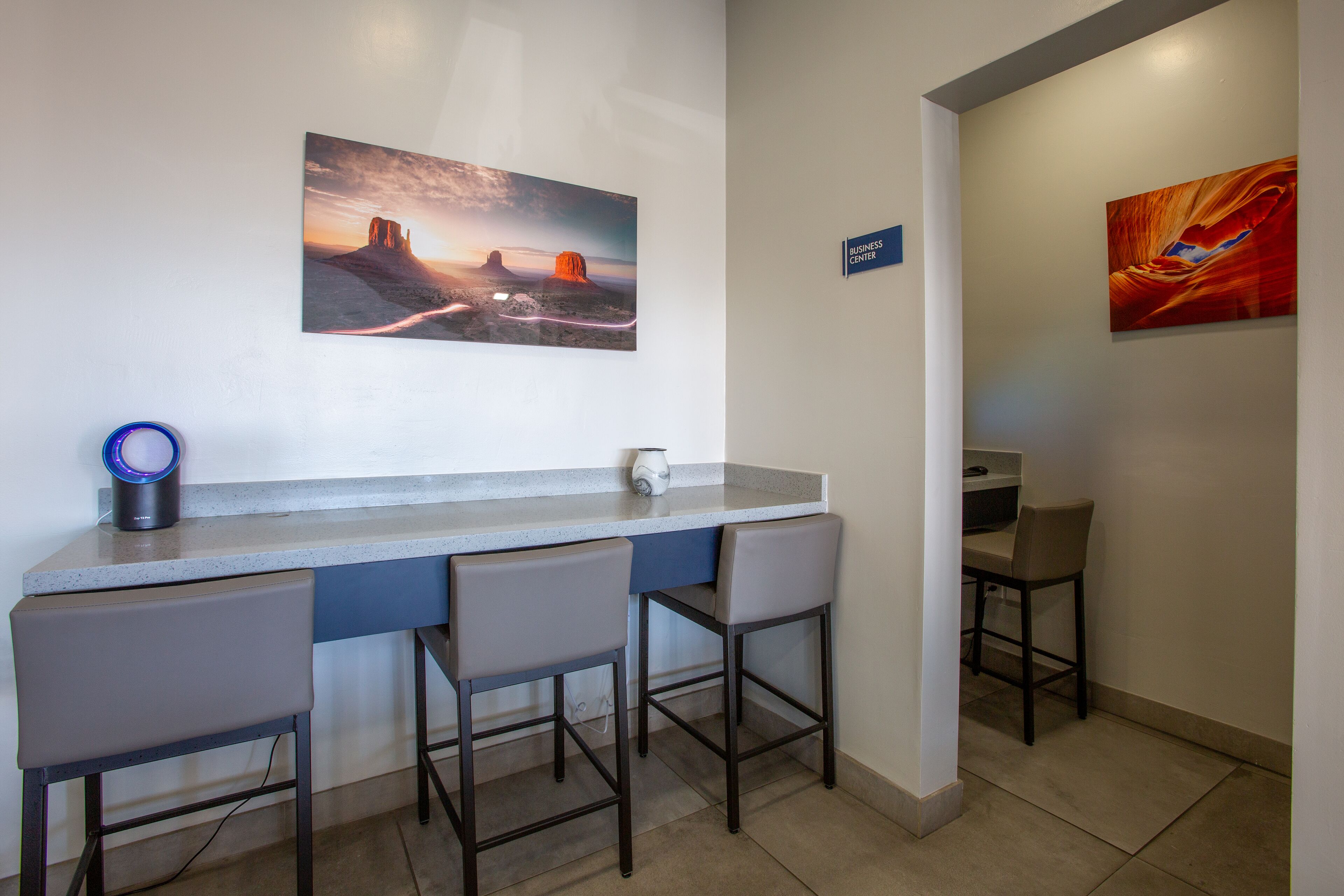 Un espace d’accueil avec un comptoir, trois tabourets de bar, deux tableaux et un panneau indiquant « Centre d’affaires ».