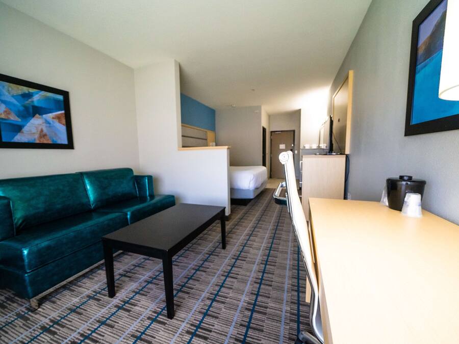 Habitación de hotel con sofá verde, una mesita, cama, escritorio con lámpara y cafetera.