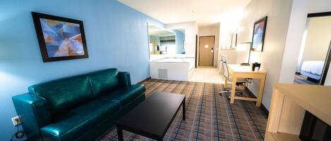 A hotel room with a green sofa, a small table, a desk, and a bed.