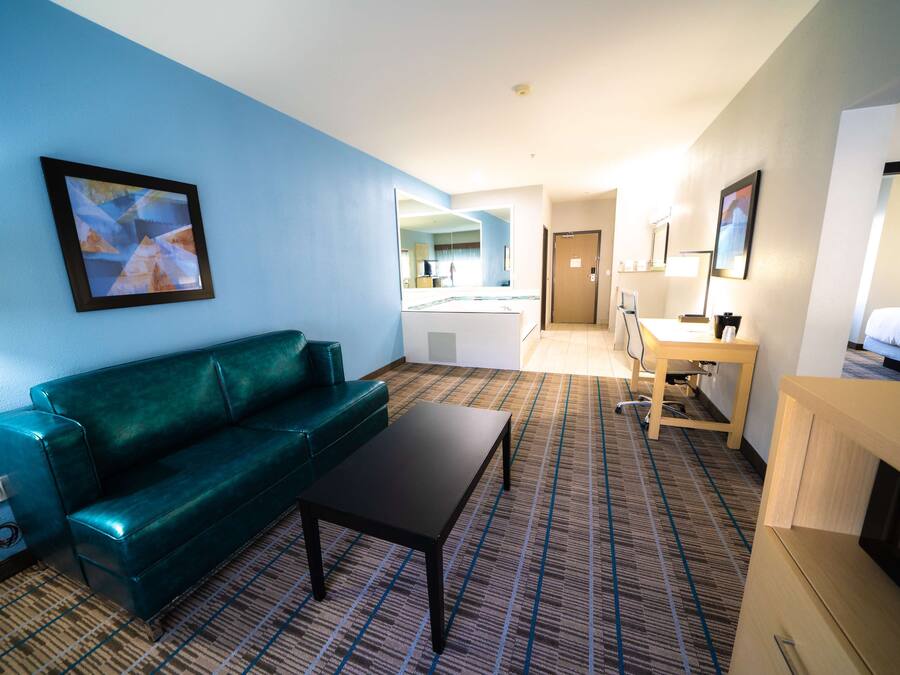 A hotel room with a green sofa, a small table, a desk, and a bed.