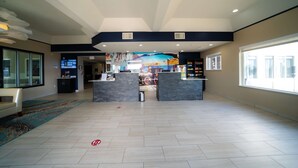 En rummelig lobby med en receptionsdisk, et stort muralmaleri og udsigt udendørs gennem et vindue.