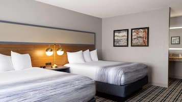 A hotel room with two beds, a wooden headboard, a nightstand with a lamp, and two framed artworks on the wall.