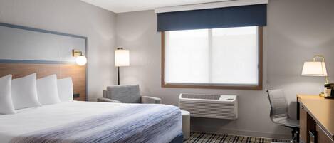 Habitación de hotel con una cama grande, un escritorio, una silla, una ventana con persianas y un aire acondicionado de pared.