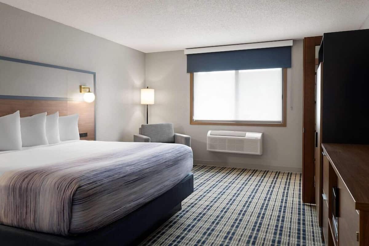 A hotel room with a bed, a chair, a desk, a television, and a window with a view.
