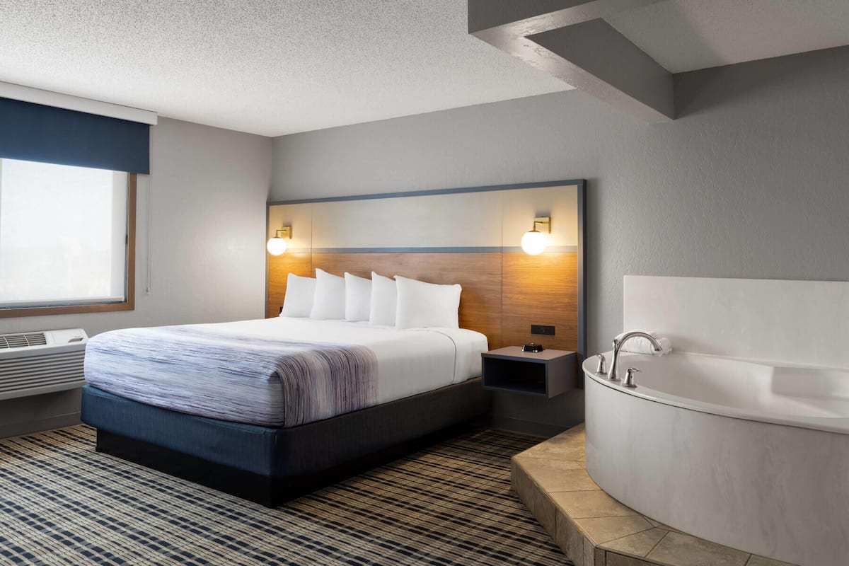 A modern hotel room with a large bed, a built-in bathtub, and a large window with a view.