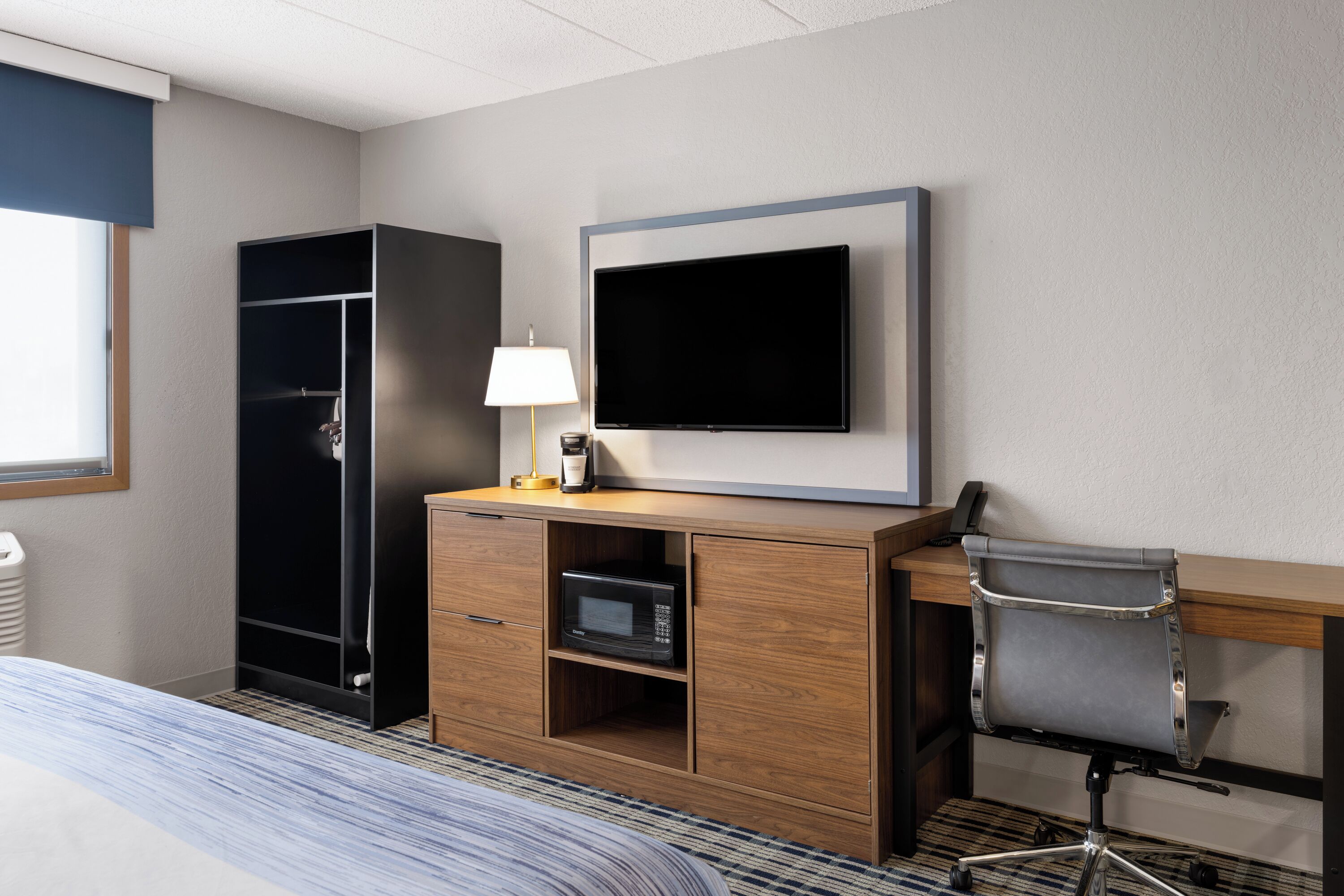 Ein Hotelzimmer mit Bett, Schreibtisch mit Stuhl, Fernseher, Kleiderschrank und Mikrowelle.