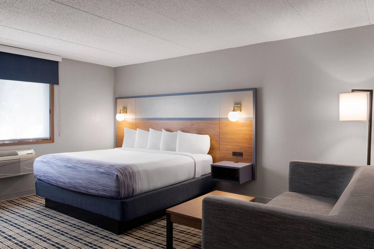 A hotel room with a bed, bedside tables, a chair, and a large window.