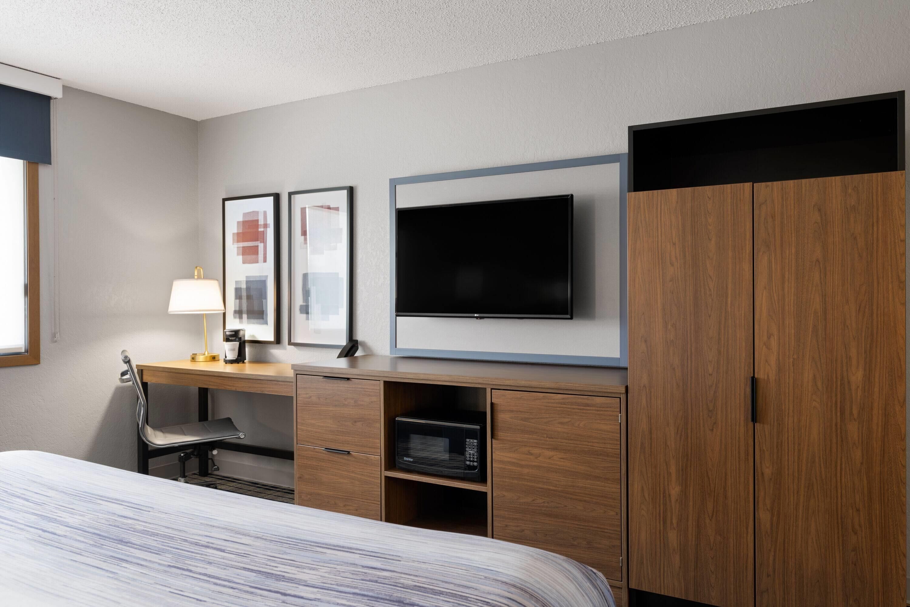 A hotel room with a bed, a desk with a lamp, a flat-screen TV, and wooden wardrobe.