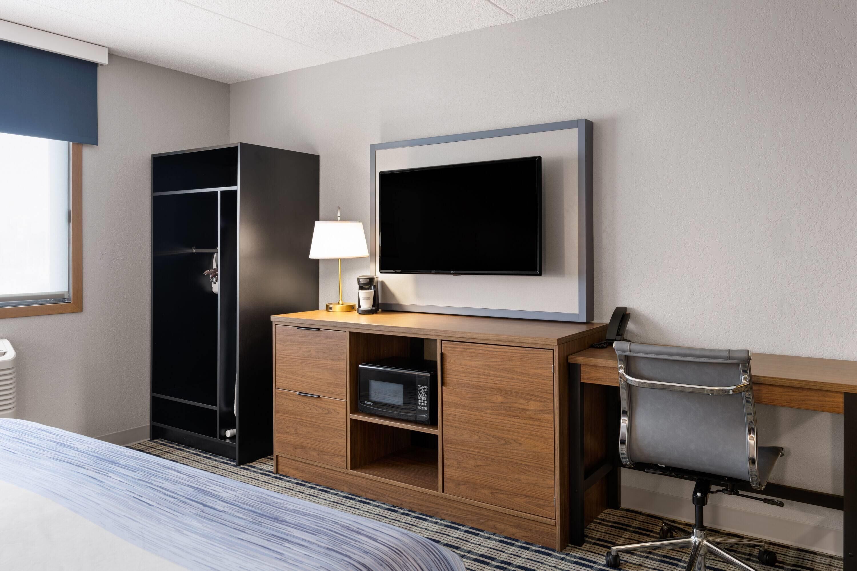 A hotel room with a bed, a desk with a chair, a television, a wardrobe, and a microwave.