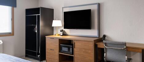 A hotel room with a bed, a desk with a chair, a television, a wardrobe, and a microwave.