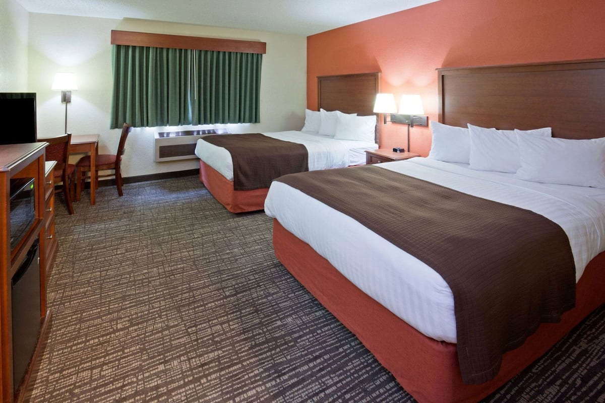 A hotel room with two beds, a desk, a chair, a TV, and a window with curtains.