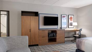 Habitación de hotel con sofá, cama, escritorio con televisor de pantalla plana, microondas y cuadros en la pared.