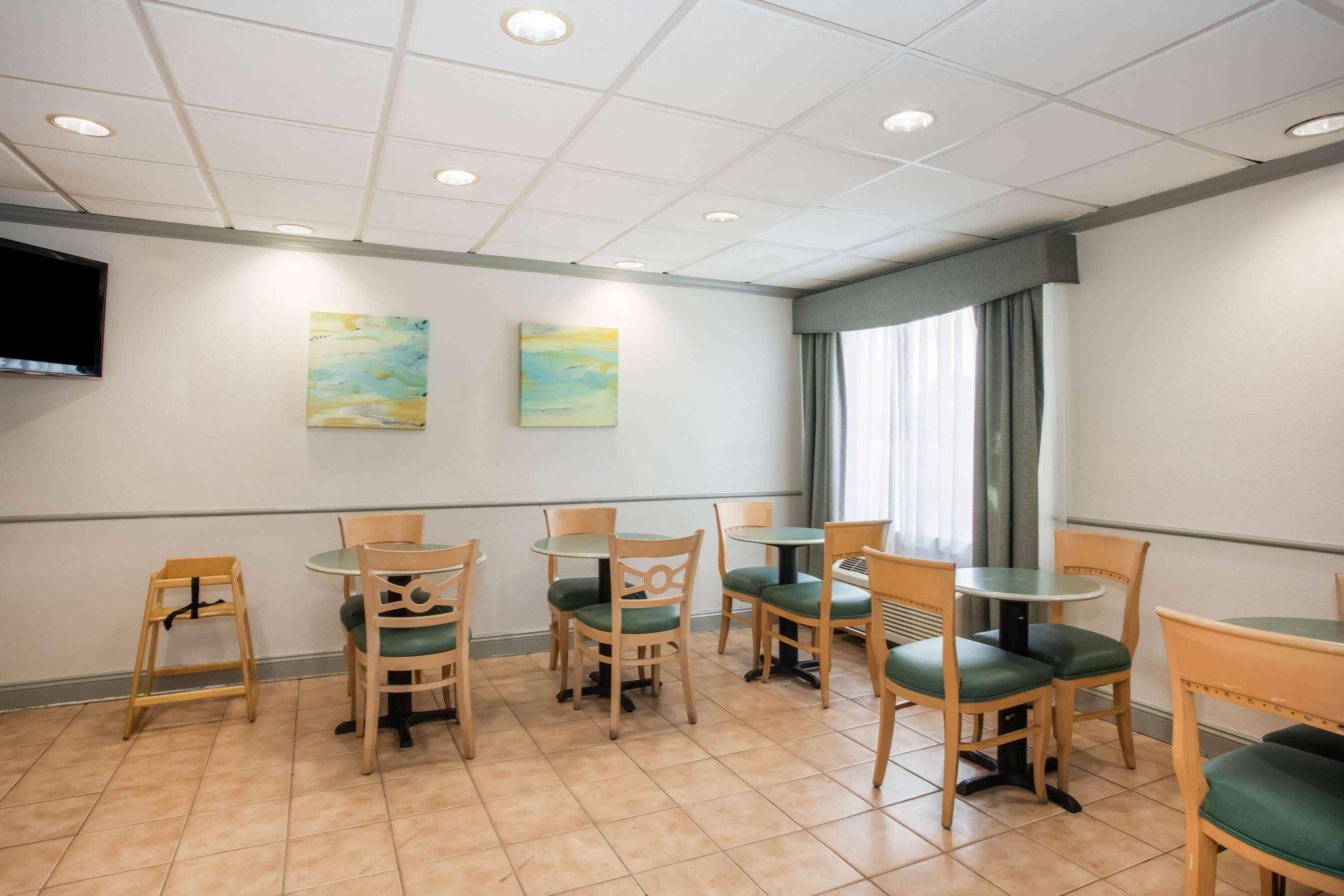A dining area with wooden chairs and tables, a flat-screen TV mounted on the wall, and two paintings.