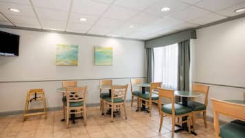A dining area with wooden chairs and tables, a flat-screen TV mounted on the wall, and two paintings.
