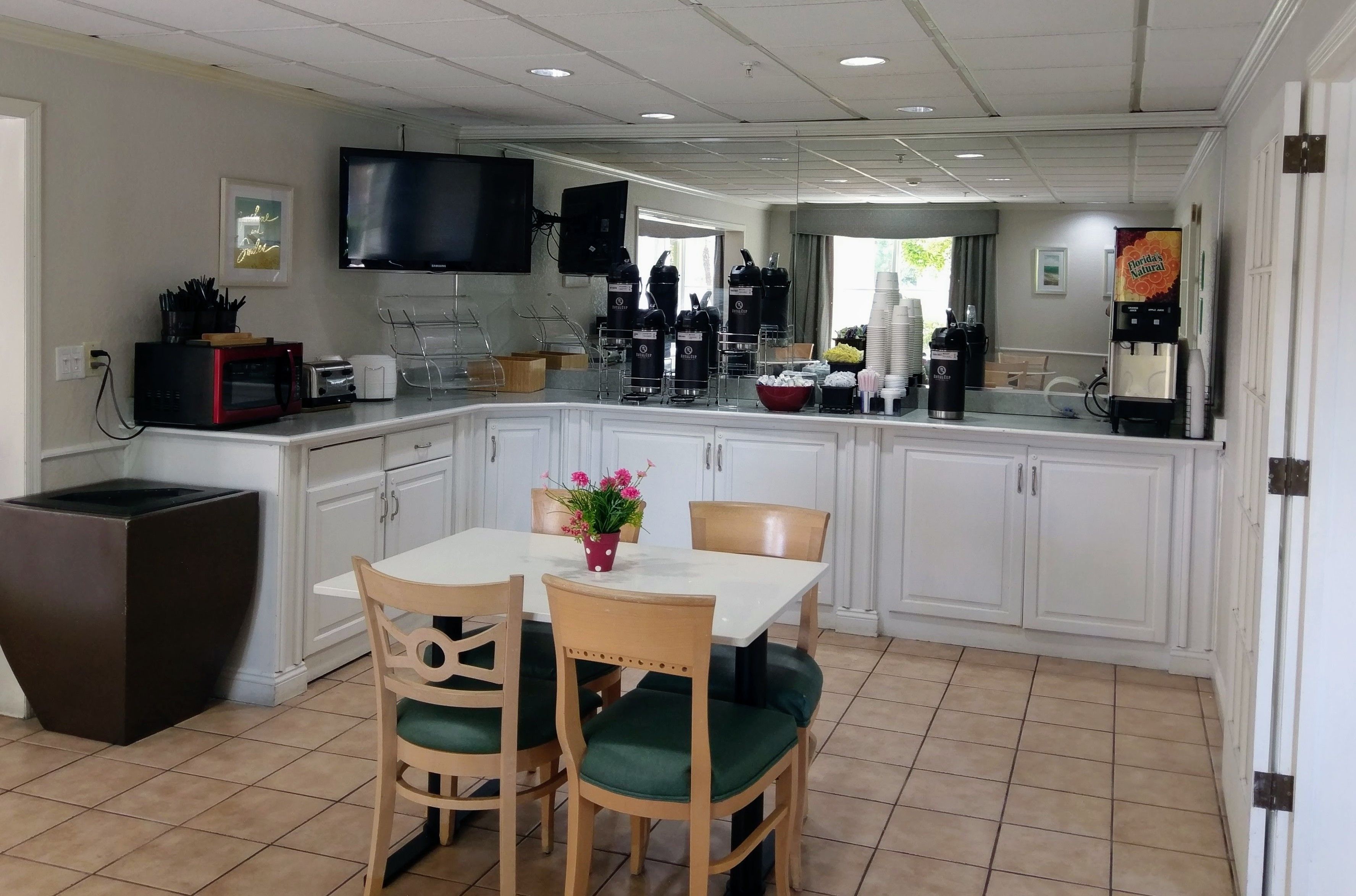 A modern kitchen with a dining area, equipped with a microwave, toaster, coffee maker, and a large TV.