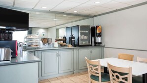 A modern kitchen with a flat-screen TV, a coffee machine, a refrigerator, and a dining area with a table and chairs.
