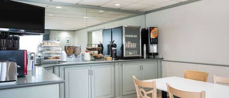 Een moderne keuken met een flatscreen-tv, een koffieapparaat, een koelkast, en een eethoek met een tafel en stoelen.