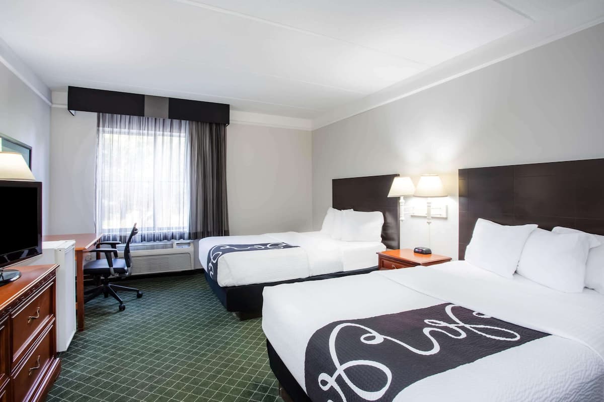 A hotel room with two beds, a desk, a television, and a window with curtains.