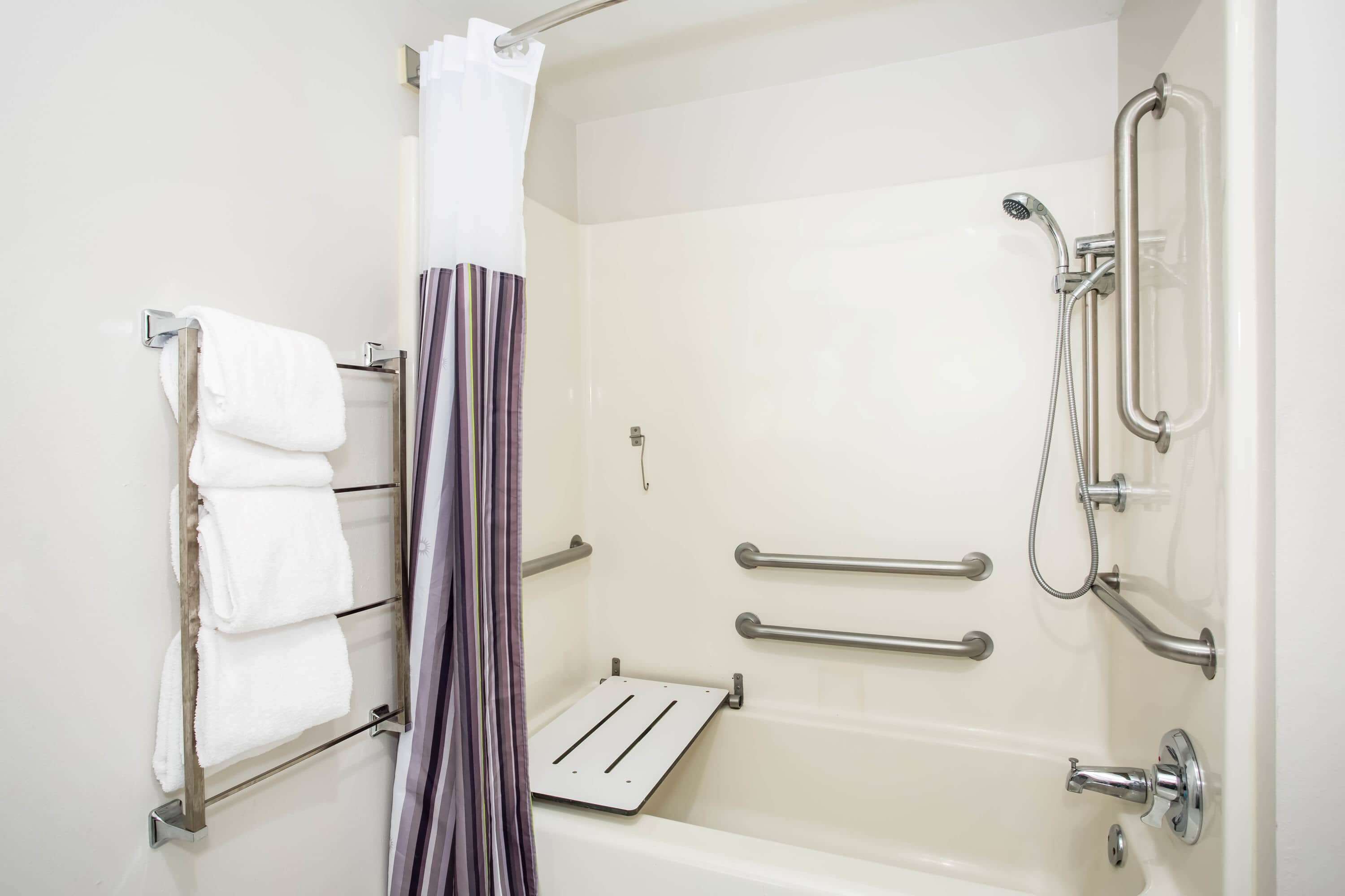Un baño con bañera, barras de apoyo, cabezal de ducha y toallero.