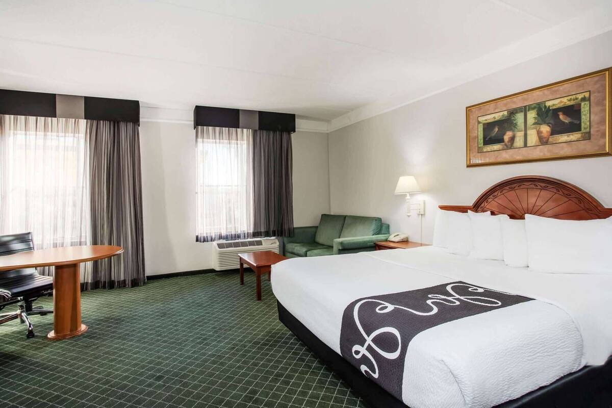 A hotel room with a bed, a desk, a chair, a sofa, and a painting on the wall.