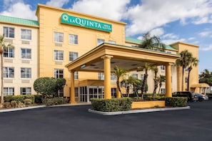 Um hotel com fachada amarela, entrada coberta e placa com a inscrição "LA QUINTA INN & SUITES".