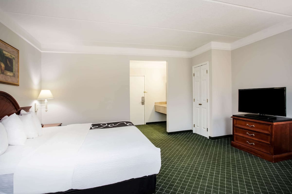 A hotel room with a bed, a television on a dresser, a lamp, and a door leading to a bathroom.