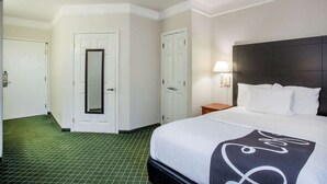 A hotel room with a bed, a nightstand, a lamp, and a mirror.