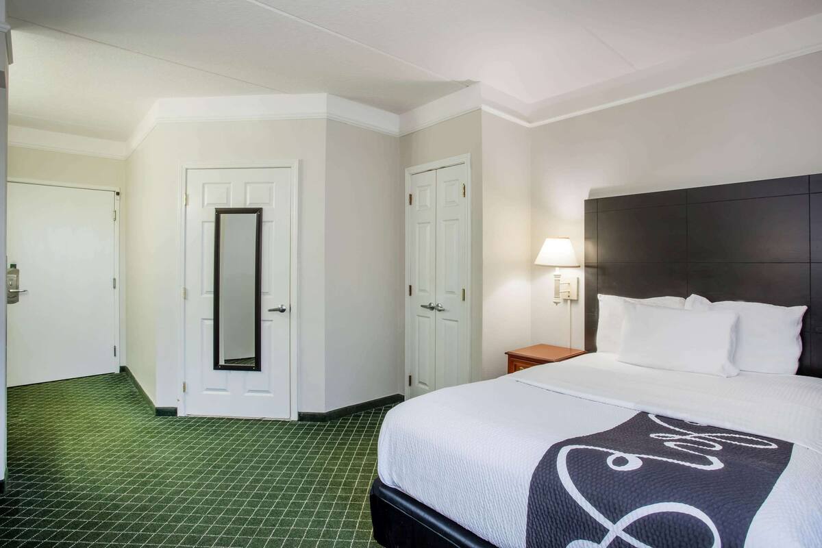 A hotel room with a bed, a nightstand, a lamp, and a mirror.