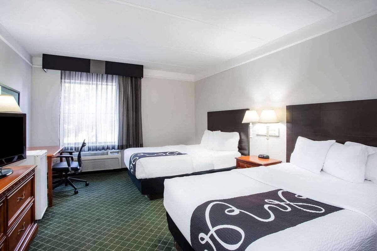 A hotel room with two beds, a desk, a TV, and a window with curtains.