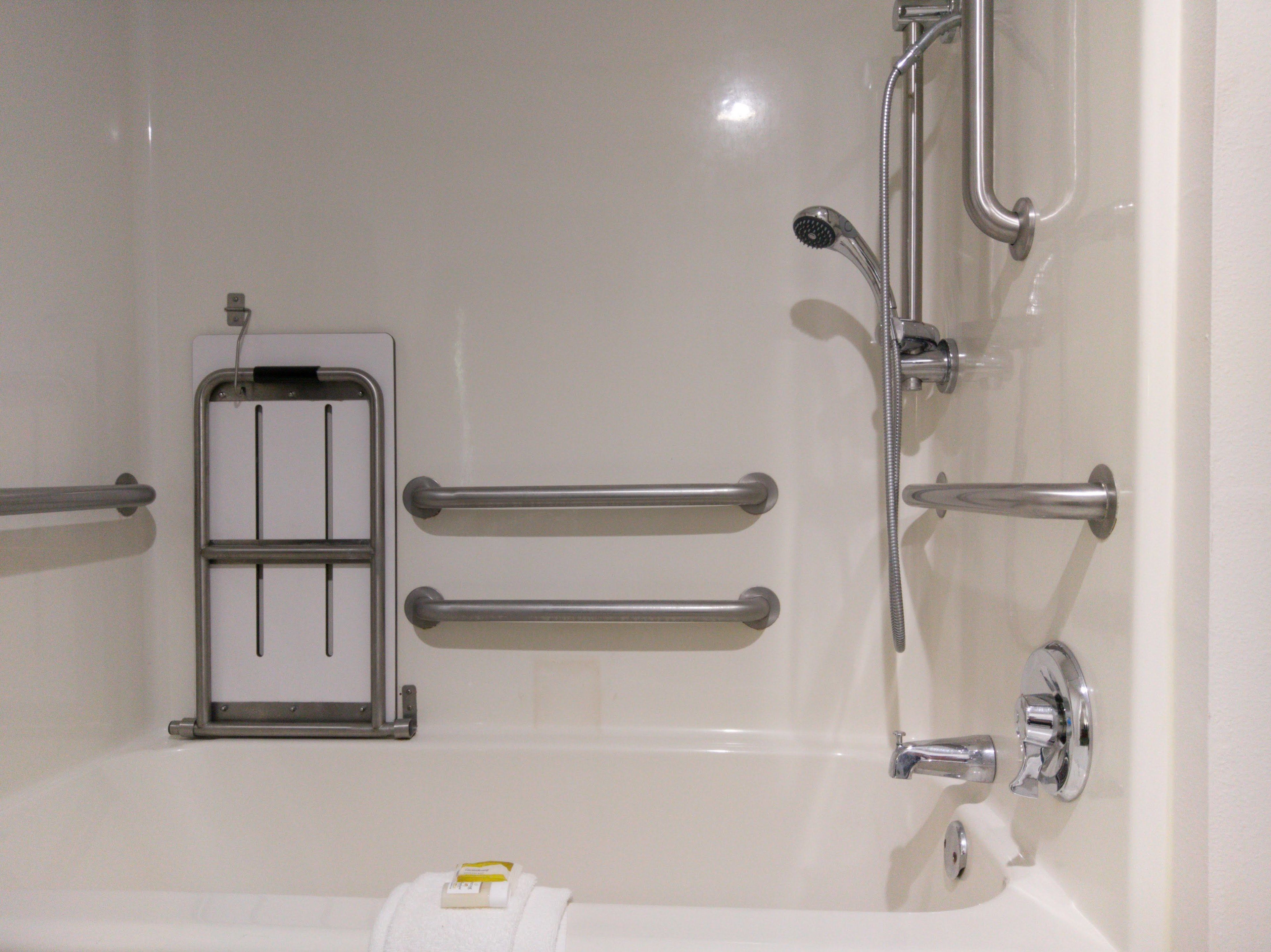 A bathroom with a bathtub, grab bars, a showerhead, and a towel dispenser.