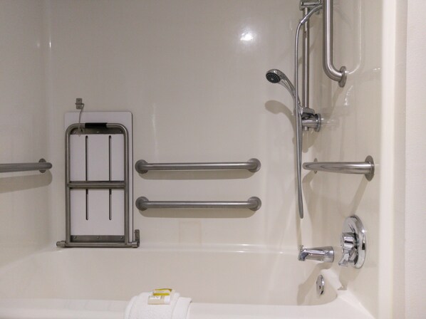 Un baño con bañera, barras de apoyo, cabezal de ducha y dispensador de toallas.