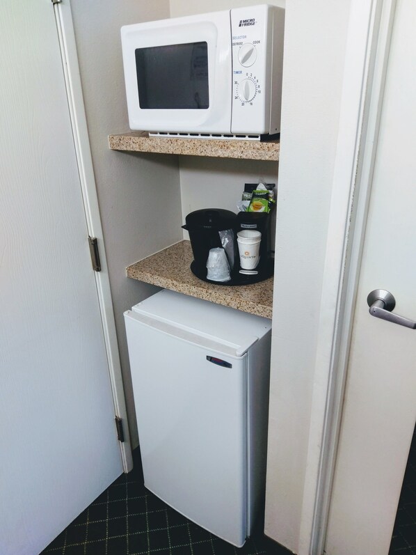 Una kitchenette compacta con microondas, cafetera y refrigerador pequeño.