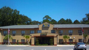 A Western Motel with a prominent office entrance, a parking lot, and a flagpole. - Western Motel Inn and Suites Hazlehurst (Hazlehurst)
