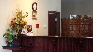 A reception desk with a wooden finish, a clock, and a framed picture on the wall. - Western Motel Inn and Suites Hazlehurst (Hazlehurst)